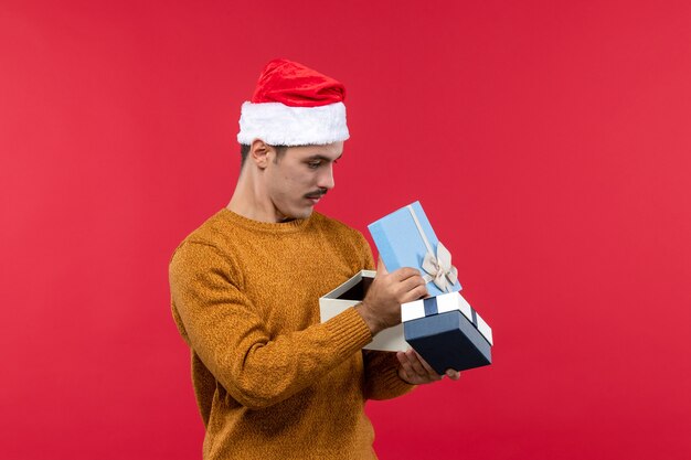 Front view of young man holding presents on a red wall