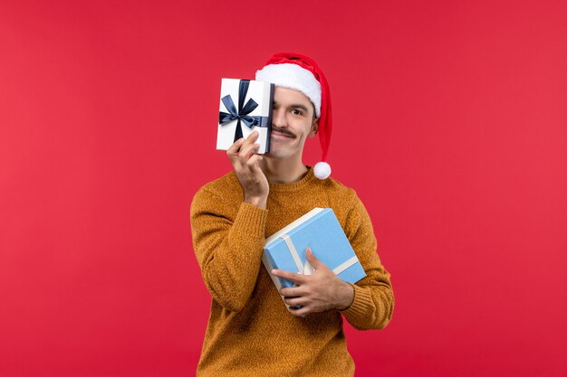 Front view of young man holding presents on red wall