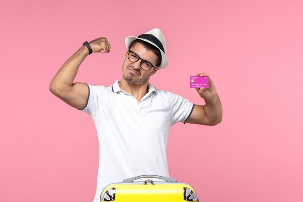 Front view of young man holding purple bank card on summer vacation on the pink wall