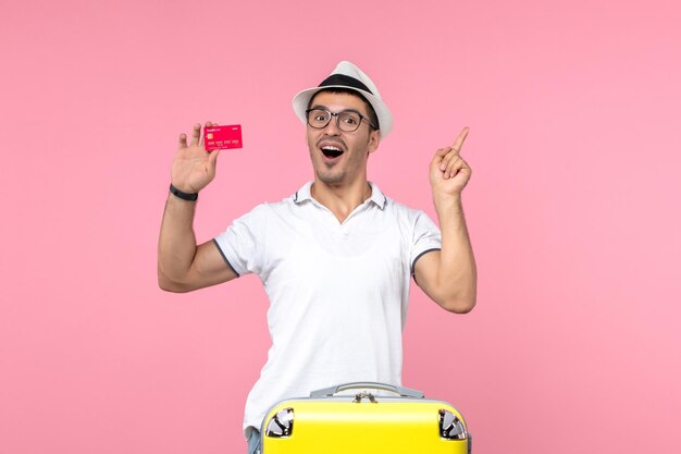 Front view of young man holding red bank card on a pink wall