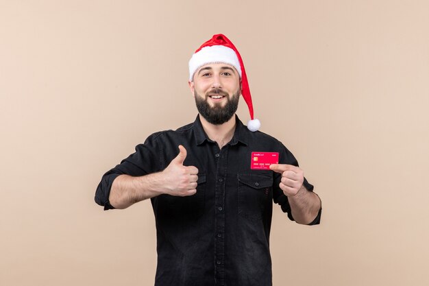 Front view of young man holding red bank card smiling on pink wall