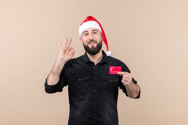 Front view of young man holding red bank card smiling on the pink wall