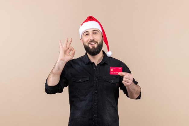 Front view of young man holding red bank card smiling on the pink wall