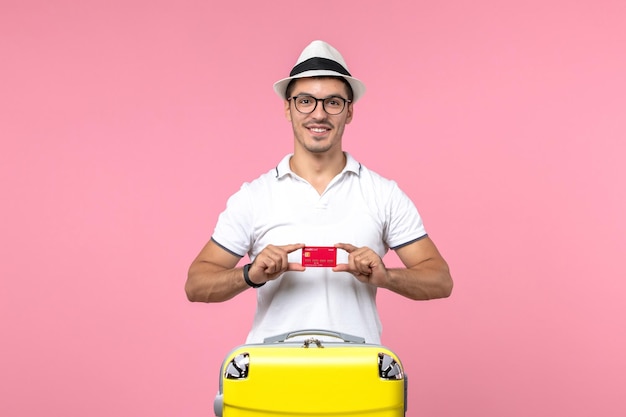 Front view of young man holding red bank card on summer vacation on pink wall