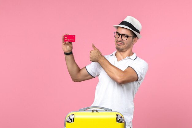 ピンクの壁に休暇で赤い銀行カードを保持している若い男の正面図