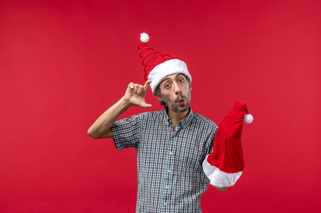 赤い壁に赤いクリスマスの帽子を保持している若い男の正面図