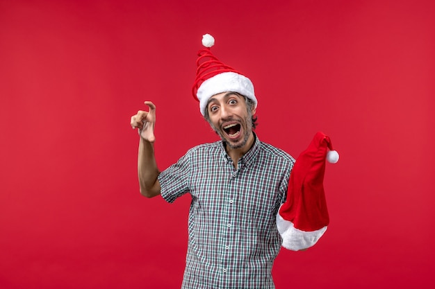 Front view of young man holding red christmas cap on a red wall