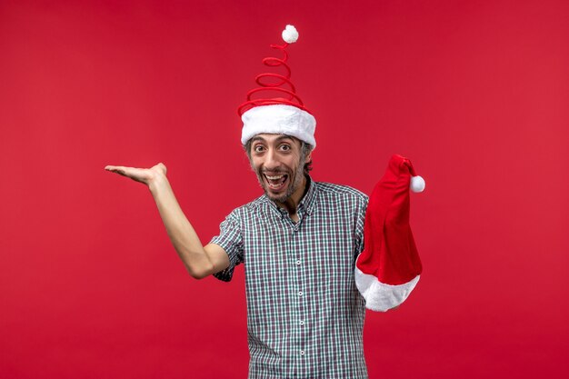 Front view of young man holding red christmas cap on red wall