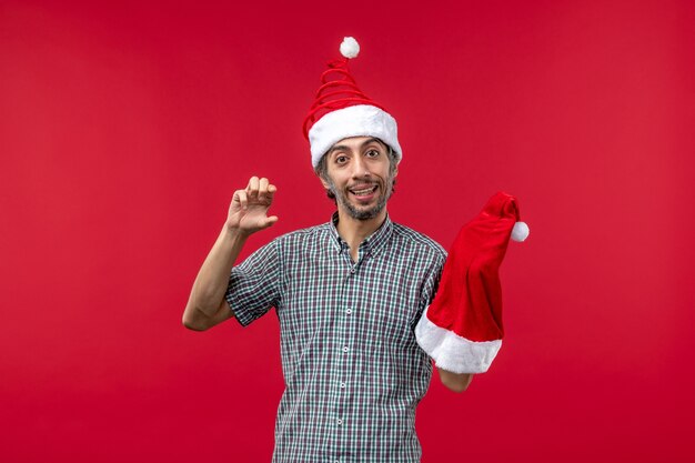 빨간 벽에 빨간 크리스마스 모자를 들고 젊은 남자의 전면보기