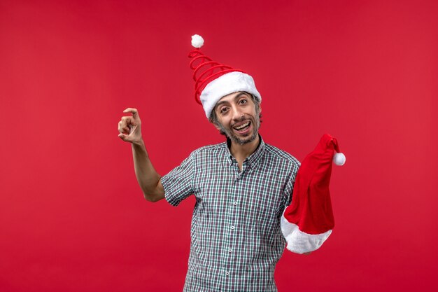 赤い壁に赤いクリスマスの帽子を保持している若い男の正面図