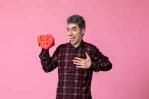 Free photo front view young man holding red heart shaped present on pink wall