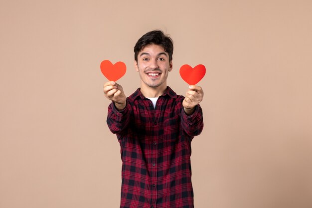 Front view young man holding red heart stickers on brown wall