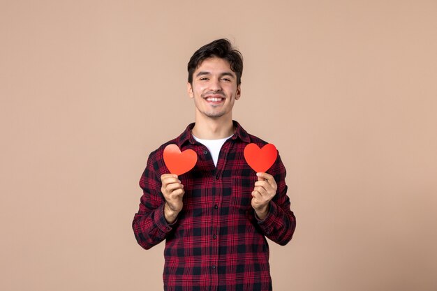 Front view young man holding red heart stickers on brown wall