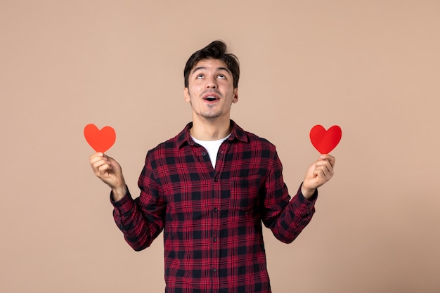 Вид спереди молодой человек, держащий наклейки с красным сердцем на коричневой стене