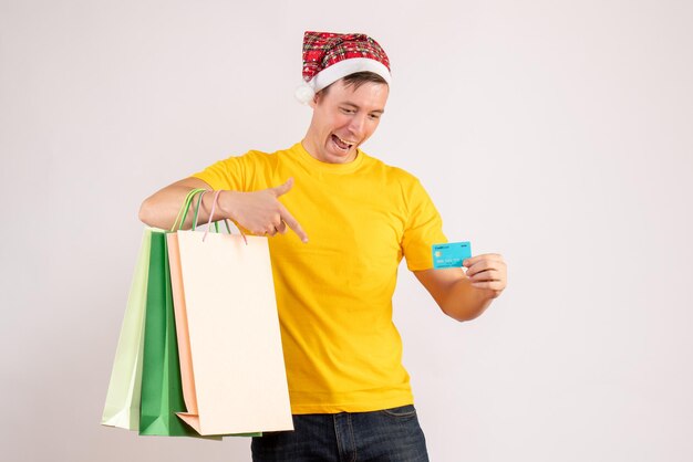 Front view of young man holding shopping packages and bank card on white wall