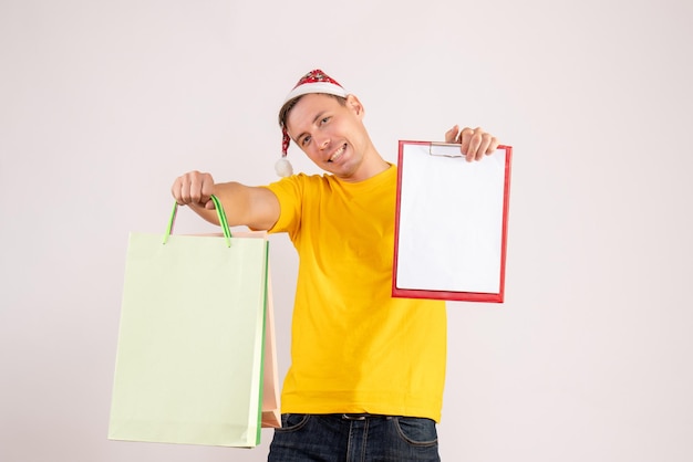 Front view of young man holding shopping packages and note on white wall