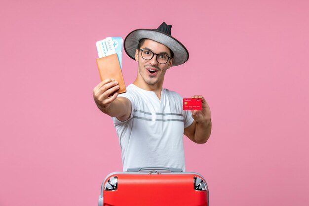 Front view of young man holding tickets and bank card on a pink wall