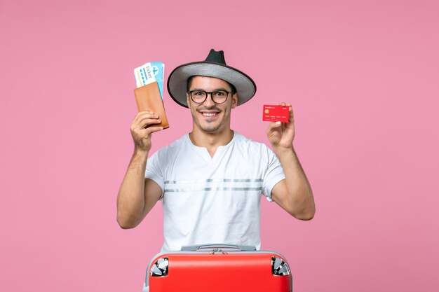 Front view of young man holding tickets and bank card on a pink wall