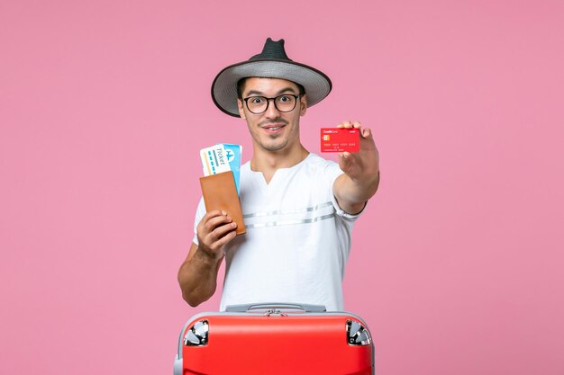 Front view of young man holding tickets and bank card on a pink wall