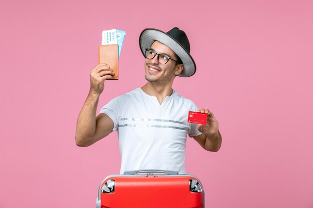 Front view of young man holding tickets and bank card on pink wall