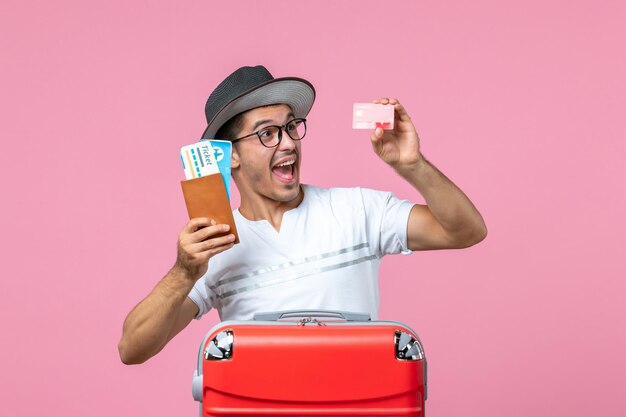 Front view of young man holding tickets and bank card on pink wall