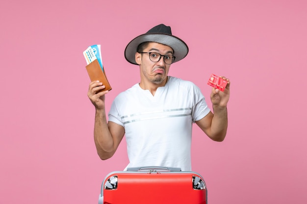 Front view of young man holding tickets and bank card on pink wall