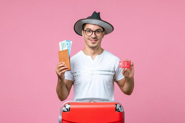 Front view of young man holding tickets and bank card on pink wall