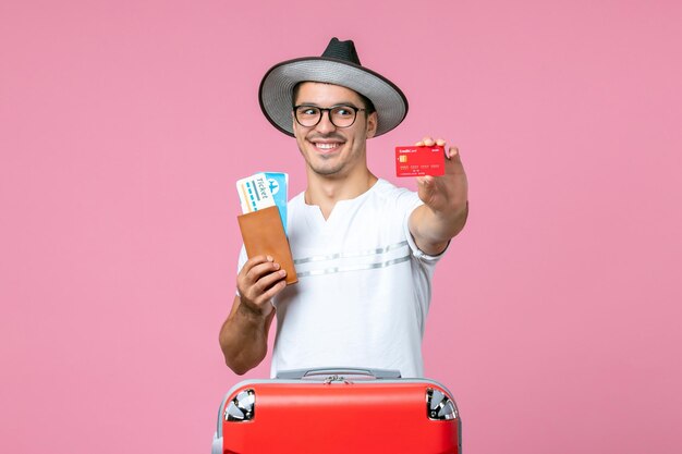 Front view of young man holding tickets and bank card on the pink wall