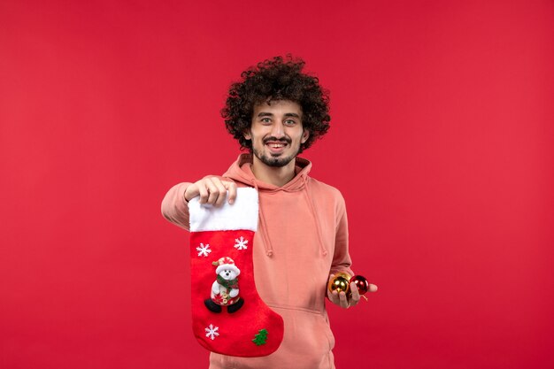 Front view of young man holding toys and sock on red wall