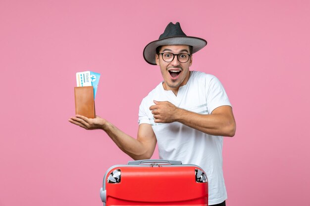 Front view of young man holding vacation tickets inside wallet on the pink wall