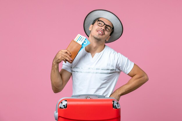 Вид спереди молодого человека, держащего отпускные билеты на розовом полу, человек в отпуске, фото, путешествие на самолете, путешествие