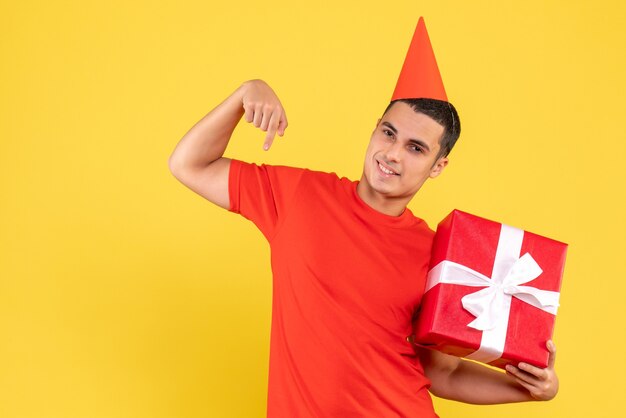 Front view of young man holding xmas present smiling on yellow wall