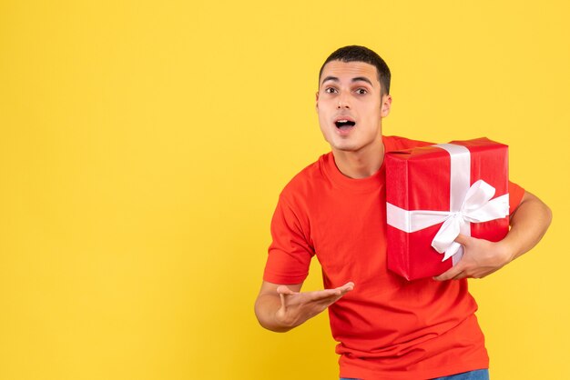 Front view of young man holding xmas present on a yellow wall