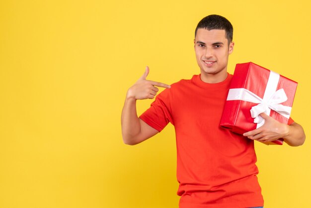 Front view of young man holding xmas present on yellow wall