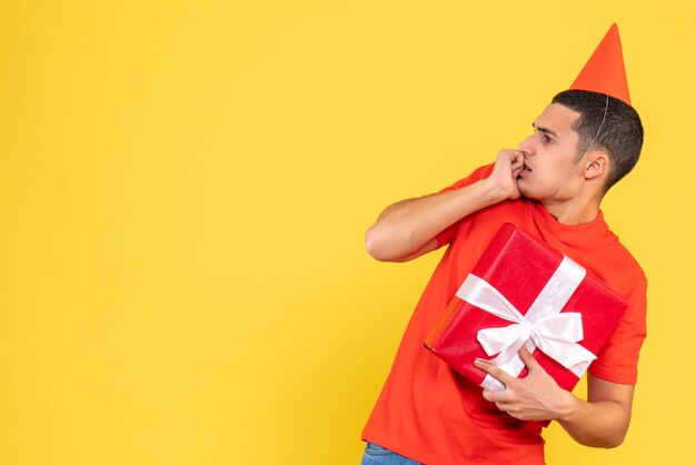 Front view of young man holding xmas present on yellow wall