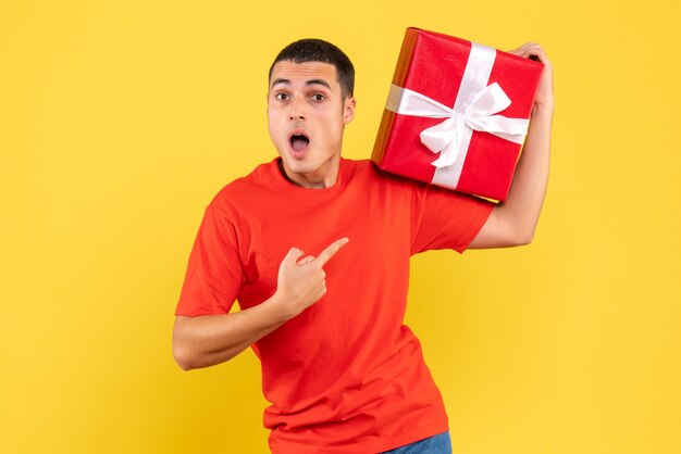 Front view of young man holding xmas present on yellow wall