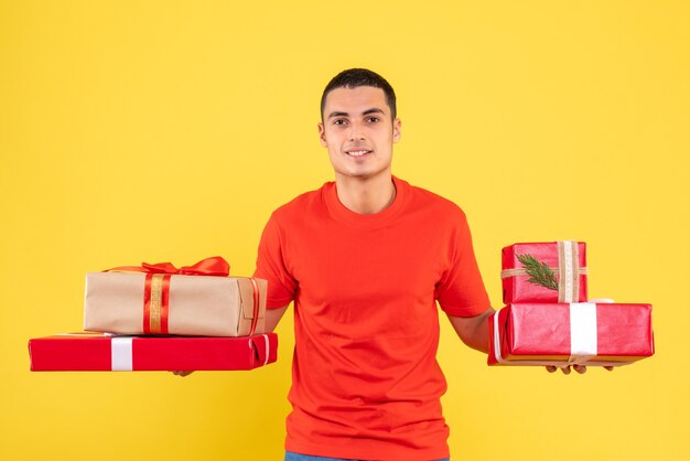 Вид спереди молодого человека, держащего рождественские подарки на желтой стене