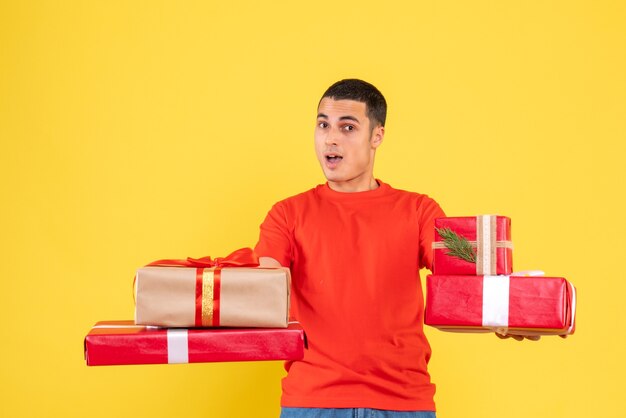 Front view of young man holding xmas presents on yellow wall