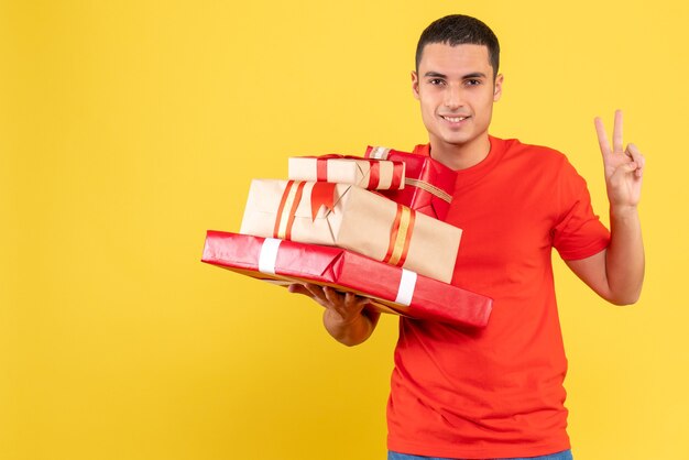 Front view of young man holding xmas presents on yellow wall