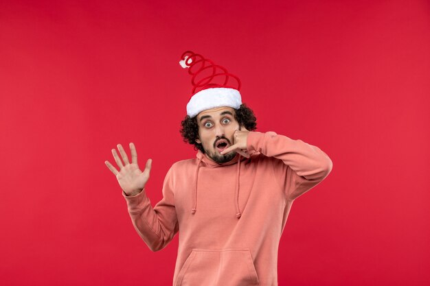 Front view of young man imitating phone call on a red wall