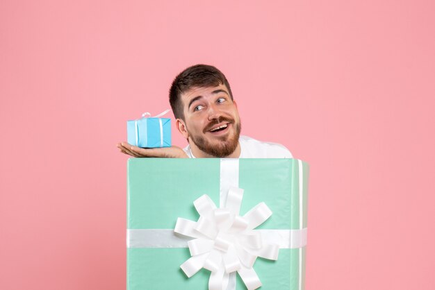 Front view of young man inside present box holding little gift on pink wall