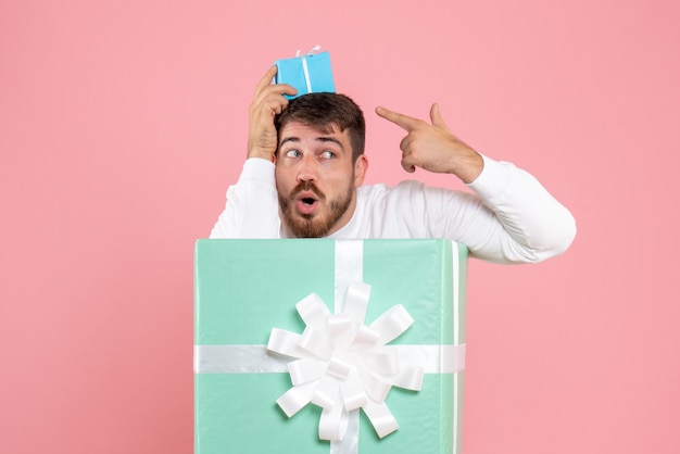 Free photo front view of young man inside present box holding little gift on pink wall