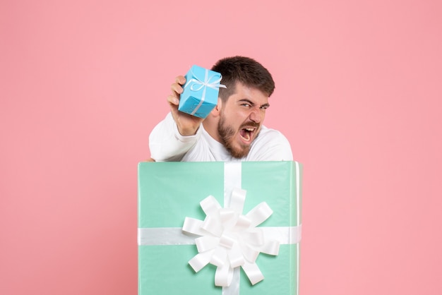 Front view of young man inside present box holding little gift with screams on pink wall