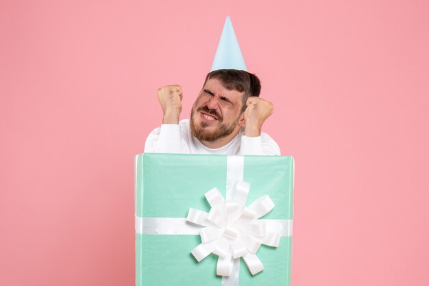 Front view of young man inside present box on a pink wall