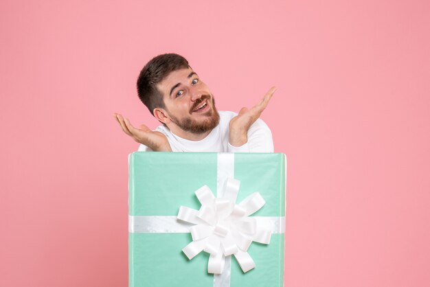 Вид спереди молодого человека внутри подарочной коробки на розовой стене