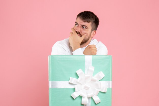 Front view of young man inside present box on pink wall