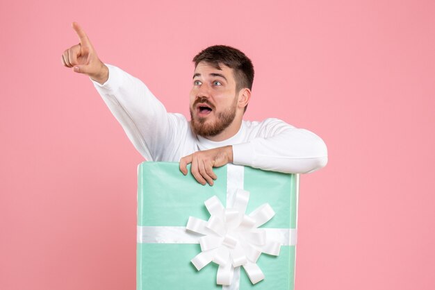 Front view of young man inside present box on pink wall