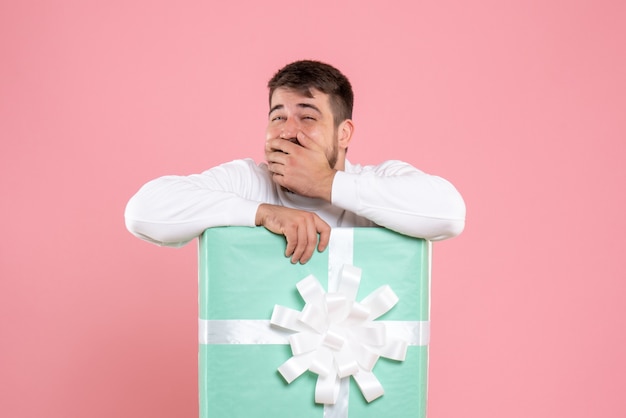 ピンクの壁のプレゼントボックス内の若い男の正面図