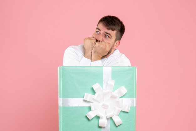 ピンクの壁に怖がっているプレゼントボックスの中の若い男の正面図