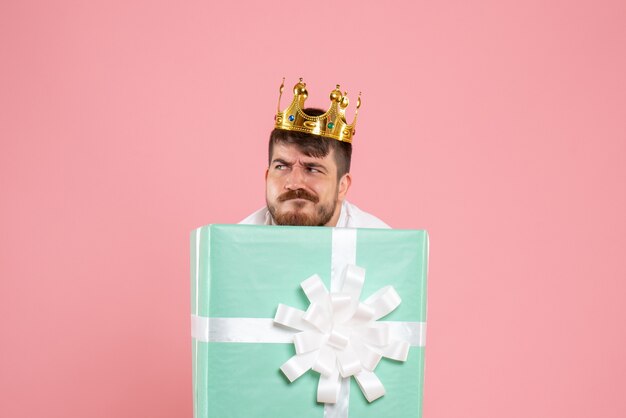 Front view of young man inside present box with crown on light-pink wall
